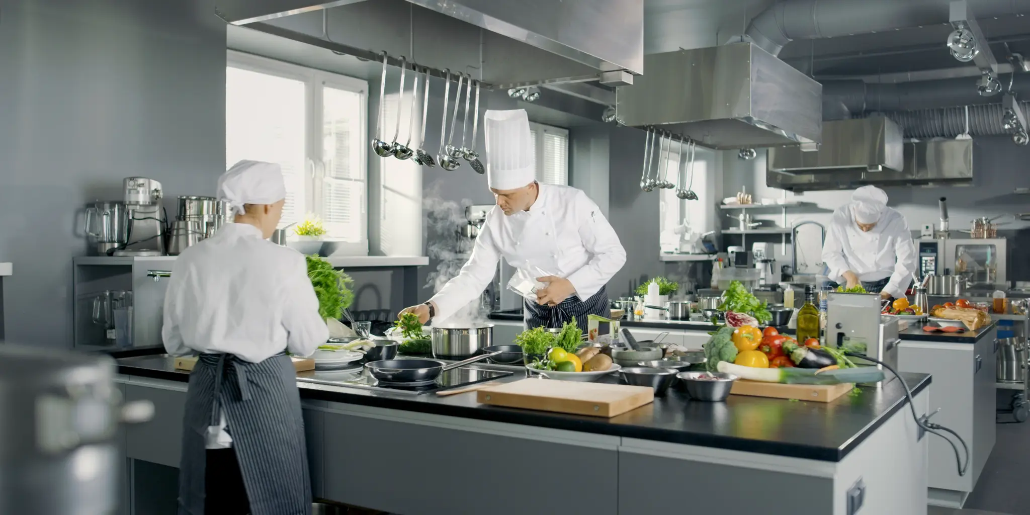 Köche bereiten in einer professionellen Küche frisches Essen mit Gemüse und Kräutern vor.